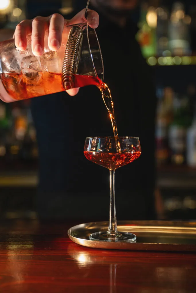 Bartender pouring the 404, a Sippers signature cocktail, into a coupe glass