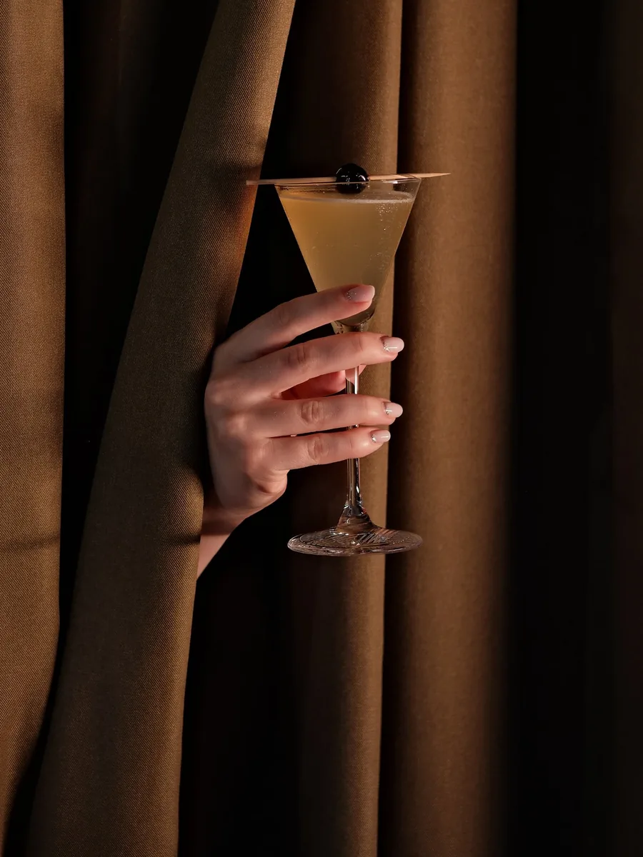 Classic cocktail held through a curtain at Sippers