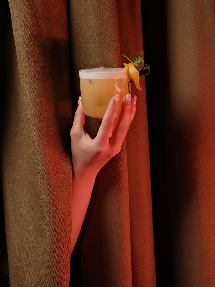Hand holding a cocktail through a copper curtain at Sippers